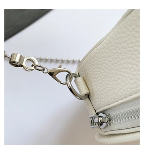 Close-up of white lychee leather texture with silver metal hardware and chain strap