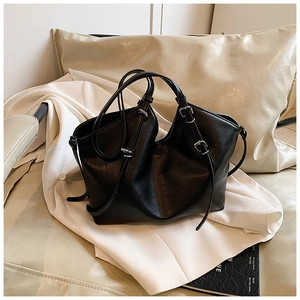 Detail of black pebbled leather tote bag with silver buckles on a beige sofa