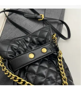 Detail of black quilted leather bucket bag with gold chain strap and diamond stitching