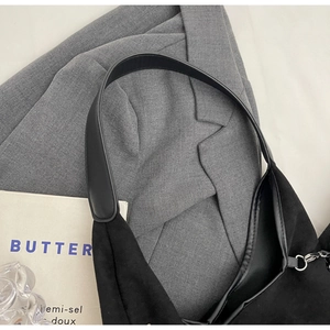 Gros plan du sac bandoulière en daim noir mat avec sangle large et boucles argentées