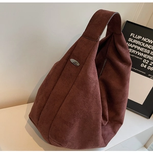 Detail of a large red-brown suede hobo bag featuring a metallic oval tag and wide strap