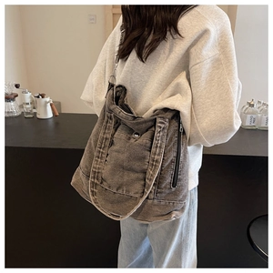 Detail of grey washed denim tote bag showing stitching and side zipper on a shoulder strap