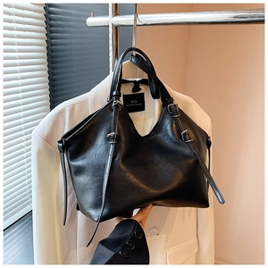 Close-up of black textured leather tote bag with silver buckles on white blazer
