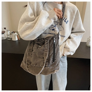 Detailed view of large charcoal denim tote bag with wide strap and zip pocket worn by model