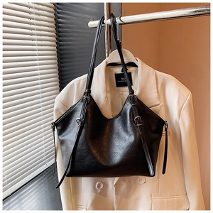 Detail view of black pebble-textured tote bag with vintage side buckles and shoulder straps