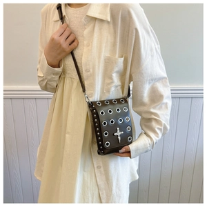Crossbody bag with silver metal eyelets and gothic cross emblem worn over beige knitwear
