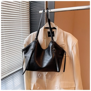 Detail of a black textured PU leather tote bag with silver buckle on a white blazer