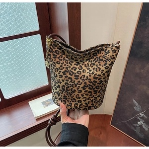 Detail of leopard print tote bag featuring brown leather handles and a gold chain accessory