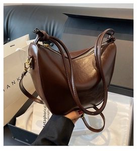 Detail of a dark brown crescent bag with glossy leather and knotted gold hardware
