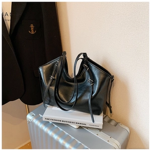 Detail of black glossy PU leather tote bag on silver suitcase with fashion book