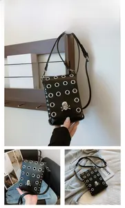 Detail of black punk mini crossbody bag with silver eyelets and metal skull badge