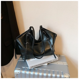Detail of glossy black faux leather tote bag with silver hardware on a metal suitcase