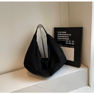 Minimalist large black suede hobo tote bag displayed on a clean white stone pedestal