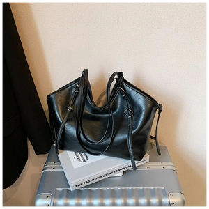 Detail of a black leather tote bag with soft texture resting on a silver suitcase