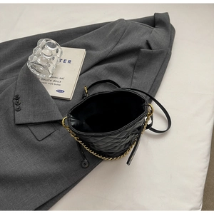 Top view of black quilted bucket bag with gold chain strap on grey blazer fabric