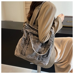 Detail of grey denim tote bag showing metal zipper closure and front utility pocket