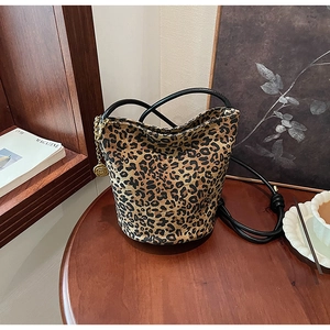 Leopard print bucket bag with long black straps and a golden rose metal charm on wood