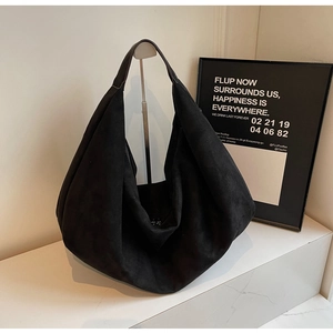 Detail of minimalist black matte hobo bag with wide shoulder strap on a sleek metal stand