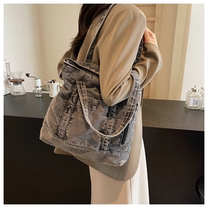 Deep grey washed denim tote bag with side zipper pocket shown on shoulder in a cafe