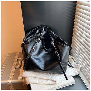 Detail view of glossy black faux leather texture and adjustable buckle strap of the tote bag
