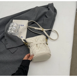 Detail shot of cream quilted bucket bag on grey suit with gold chain strap
