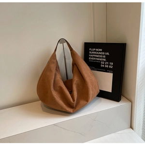 Detailed view of caramel brown suede hobo bag on marble surface with soft lighting