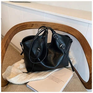Detail view of black vintage leather tote bag with adjustable silver buckle strap on a chair