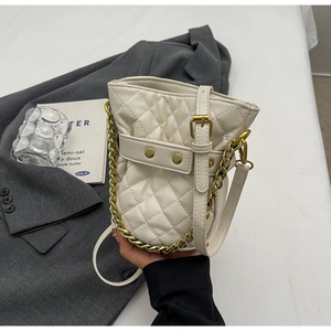 Detailed view of quilted beige bucket bag with gold chain and studded leather straps