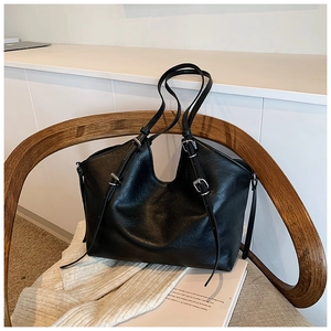 Detail of a large black vintage tote bag in soft leather texture on a wooden chair