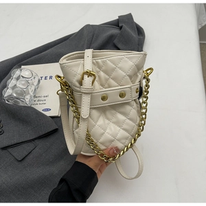 Detail of cream quilted bucket bag featuring gold chain handle and drawstring closure