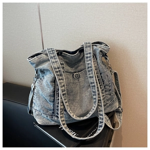 Detail of blue washed denim tote bag with metal buckles and adjustable shoulder strap