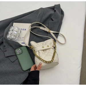 Close-up of cream quilted bucket bag with gold chain and strap on grey blazer