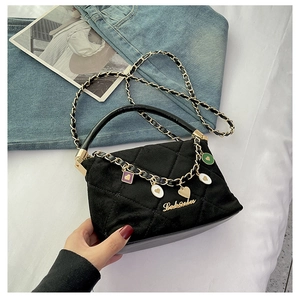 Detail of black quilted suede handbag with gold chain strap and colorful charms
