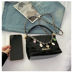 Detail of black quilted handbag with heart charms and golden chain on white fabric