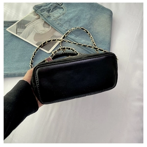 Detail view of the black crossbody bag showing its chain strap and leather bottom texture