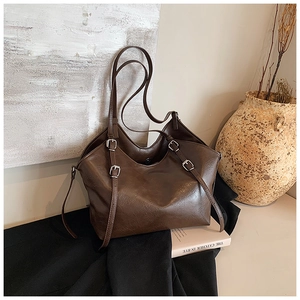 Detail of a dark brown glossy leather tote bag featuring silver metal buckles and straps
