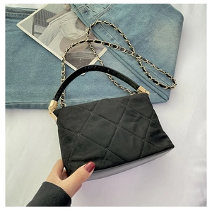 Detail of black quilted leather handbag with gold hardware and woven chain strap