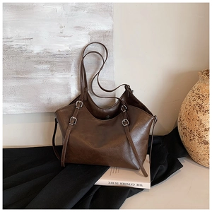 Detail view of large dark brown retro tote bag with silver buckle straps on a minimalist background