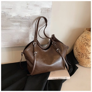 Detail view of a vintage dark brown tote bag with metal buckles on a textured fabric