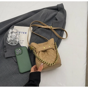 Detailed view of khaki quilted bucket bag with gold chain strap on grey blazer