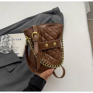 Macro detail of brown quilted bucket bag with golden chain and faux leather texture