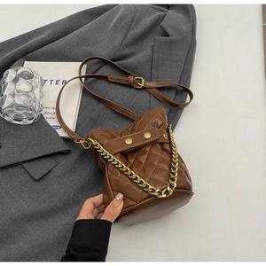 Detail of a brown quilted bucket bag with gold chain and strap on a gray blazer