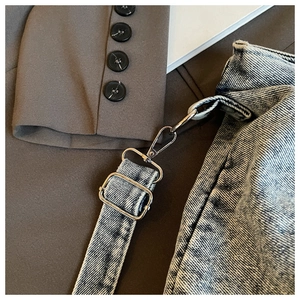 Detail of adjustable metal buckle and spring hook on light blue denim tote bag