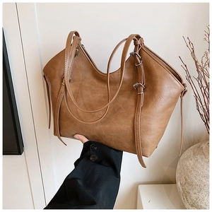 Detail of a brown leather tote bag showing soft texture and adjustable metal buckle