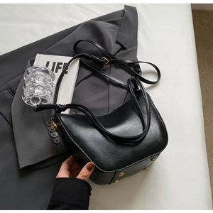 Detail of black leather hobo bag with knotted strap and gold hardware on grey blazer