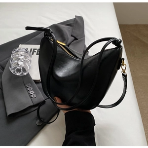 Detail of black faux leather half-moon bag with gold zipper and double thin straps