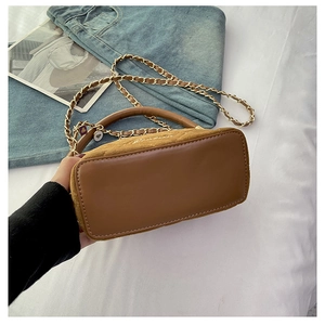 Detailed view of brown quilted handbag with gold chain strap on denim fabric