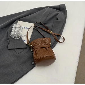 Top-down view of brown quilted bucket bag with chain strap on a grey suit background