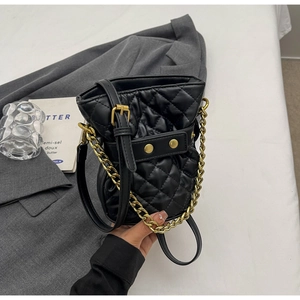 Close-up of black quilted bucket bag featuring gold chunky chains and fine leather strap