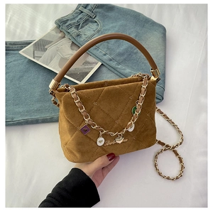 Detail of brown quilted suede bag with colorful charm chain on white linen surface